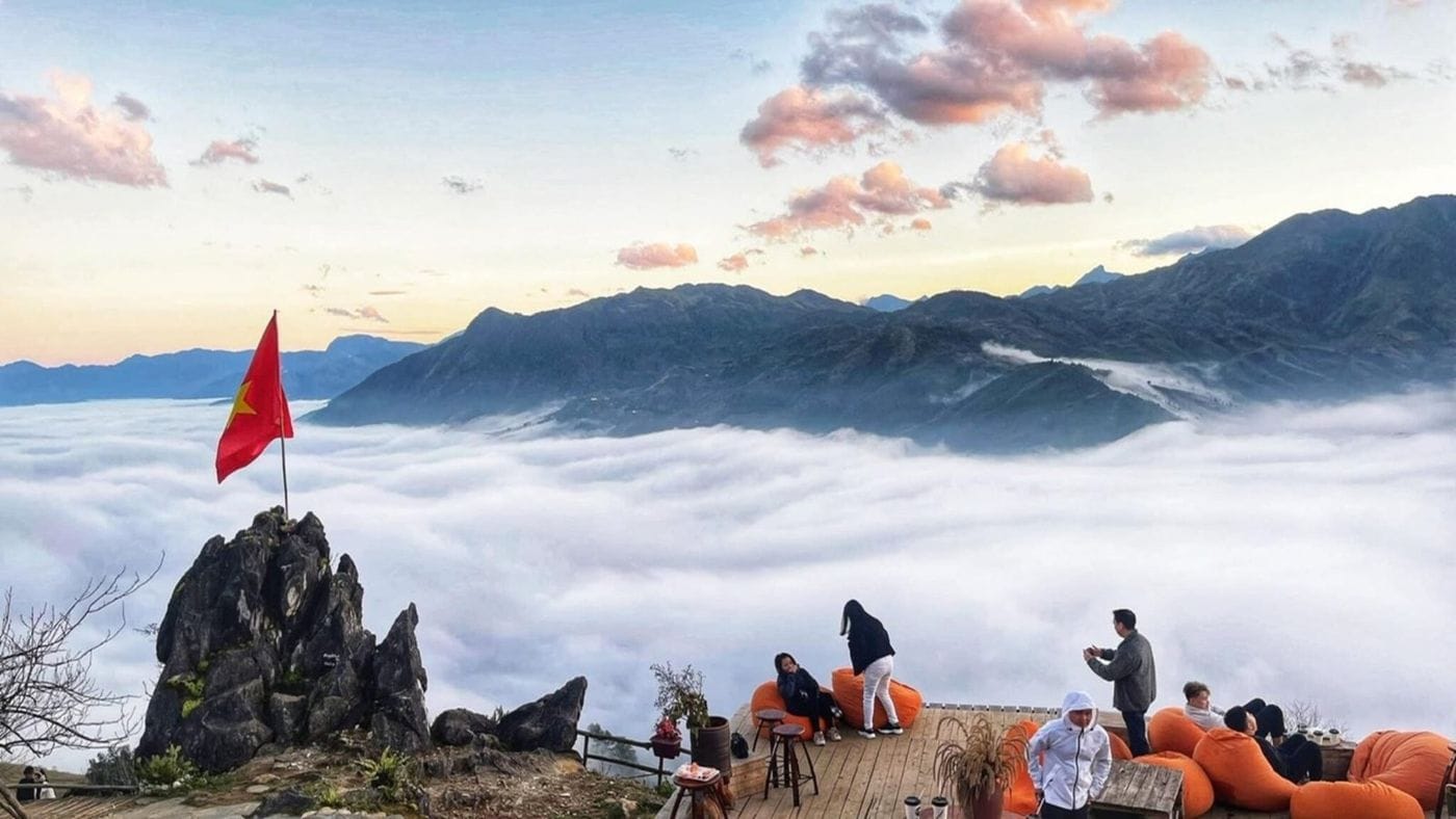 Guests on the Best View wooden deck above a sea of clouds, beside the rock with the Vietnamese flag.