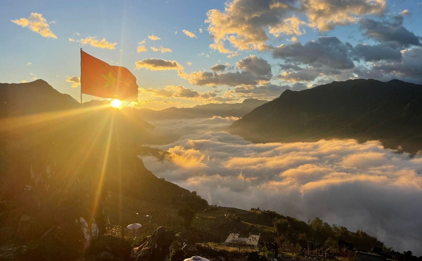 Sunrise behind the flag on the rock, with golden cloud filling the valley.