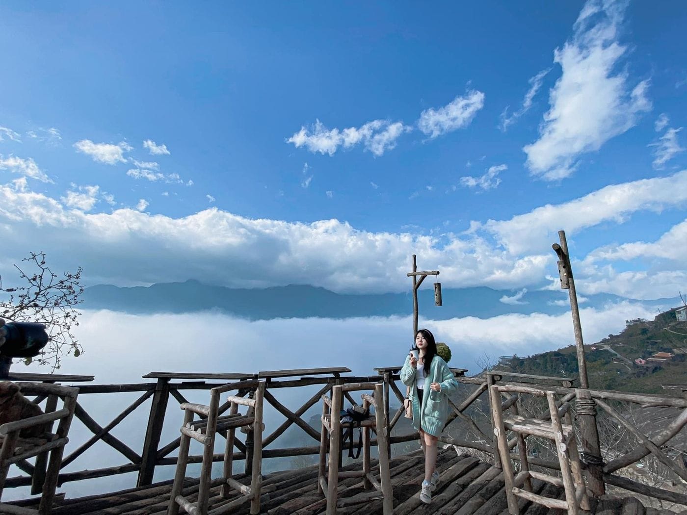 A young woman posing on the wooden deck against white cloud and blue sky.