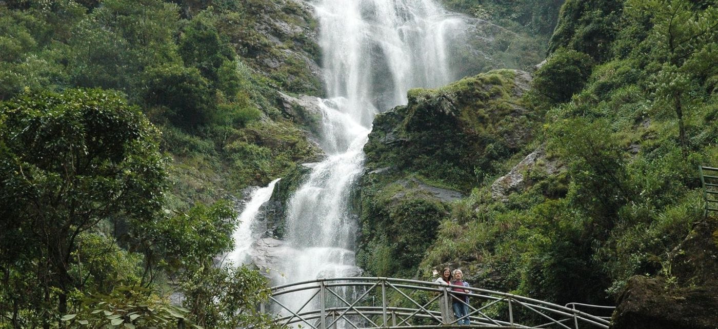 Silver Waterfall pouring white over several rock tiers amid green forest, with the iron footbridge below.