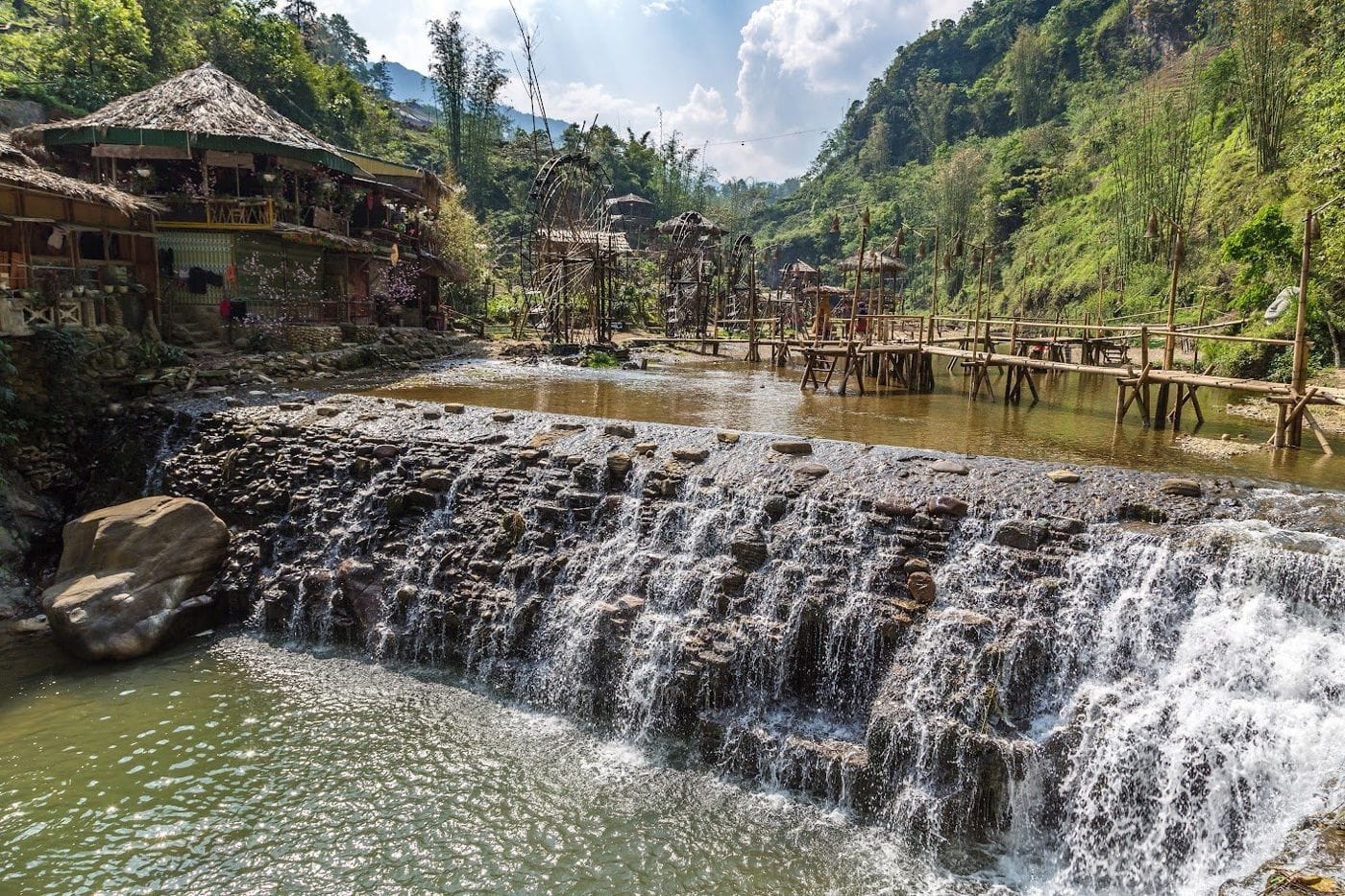 The stone weir on the Cat Cat stream, with water wheels, bamboo walkways and thatched houses behind.
