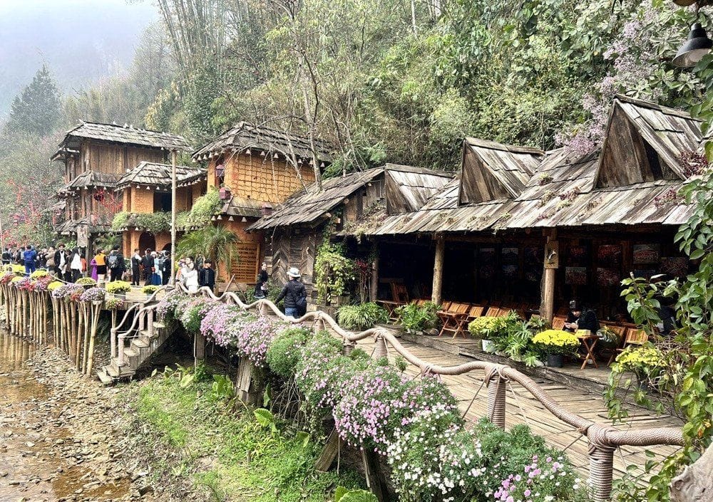 Hmong wooden houses with shingle roofs along a flower-lined path by the stream.
