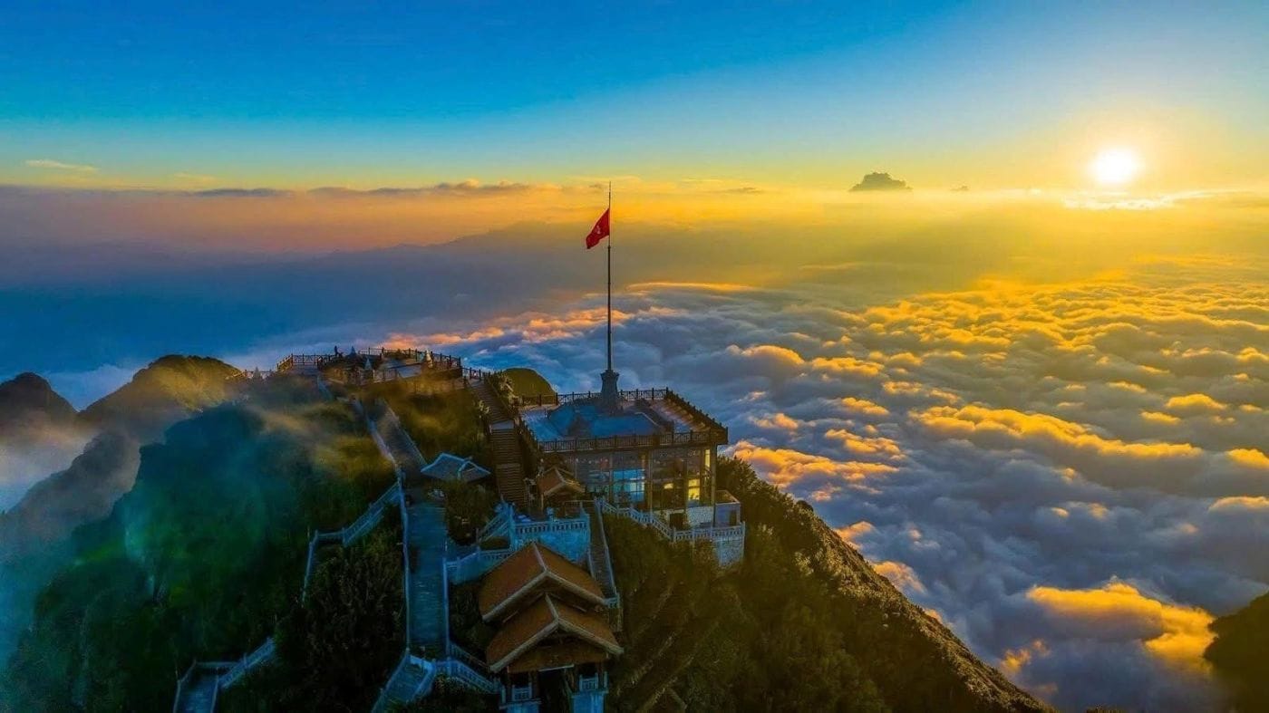 Sunrise over a sea of clouds, with the flagpole and buildings on the Fansipan summit.