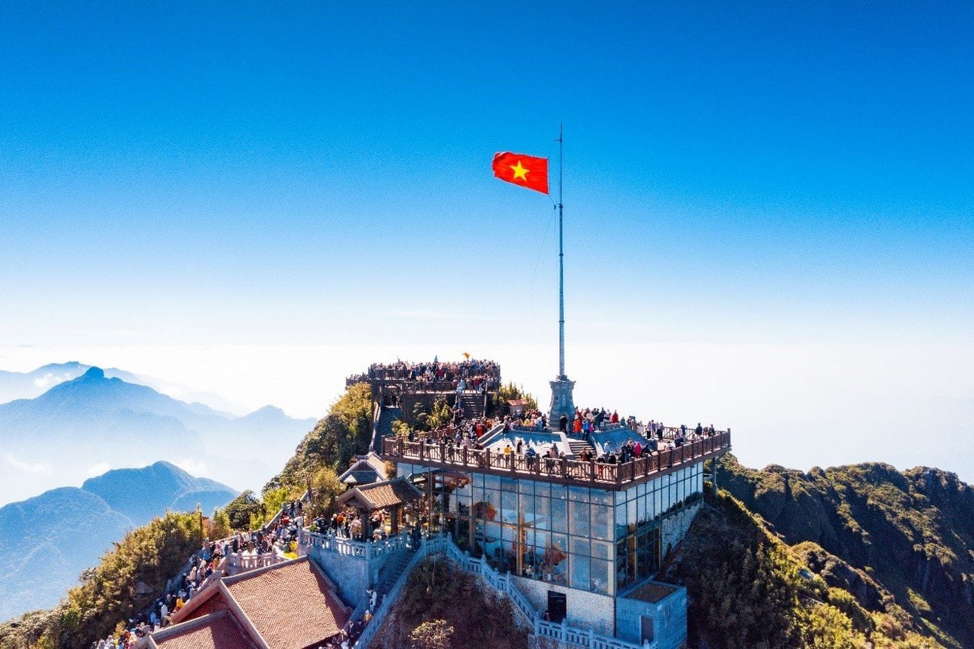 The Fansipan summit with the national flagpole and crowds of visitors under a blue sky.