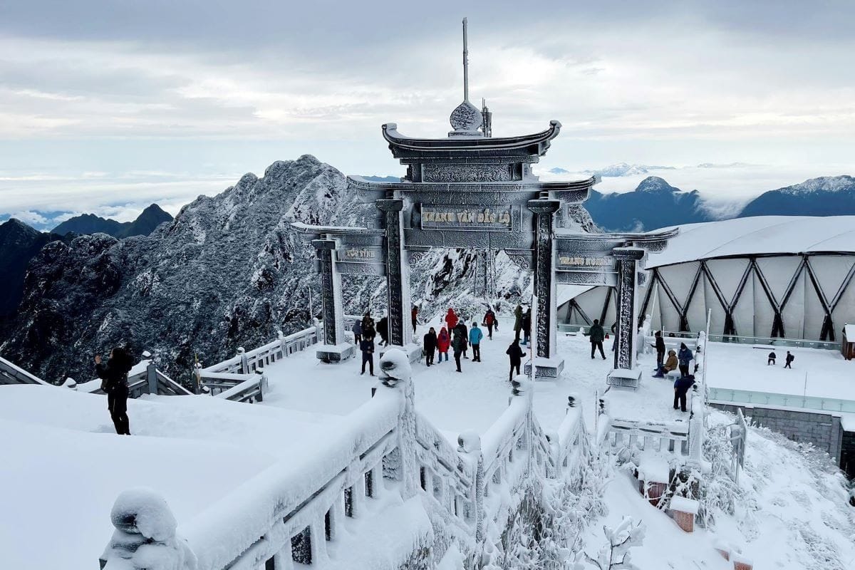 The temple gate on Fansipan covered in snow, with visitors walking around.