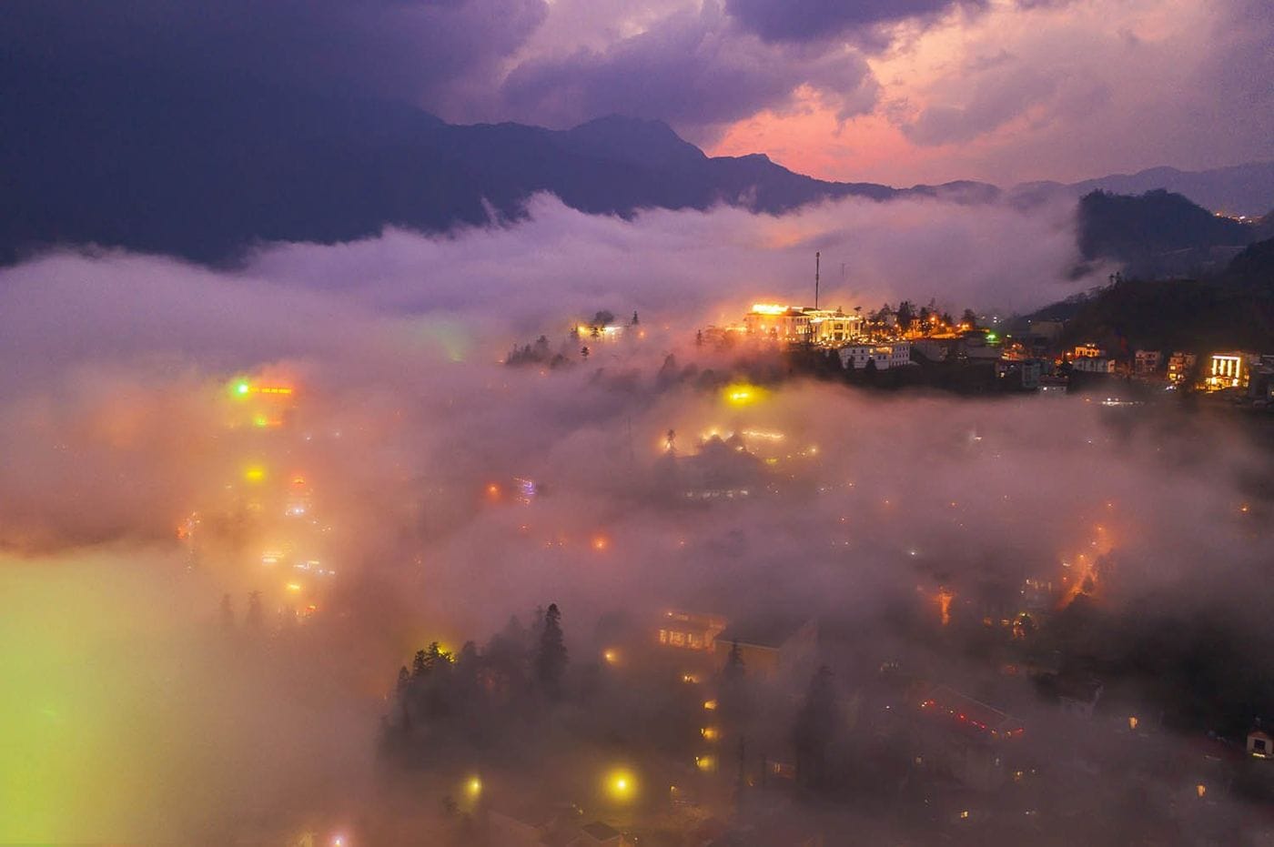 Sa Pa town lit up beneath a layer of cloud at dusk.