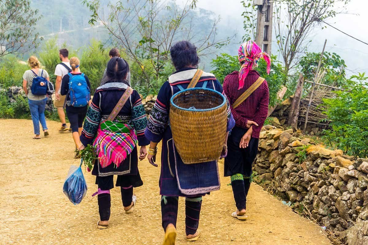Trekkers walking with Hmong women carrying baskets along a dirt path into Lao Chai.