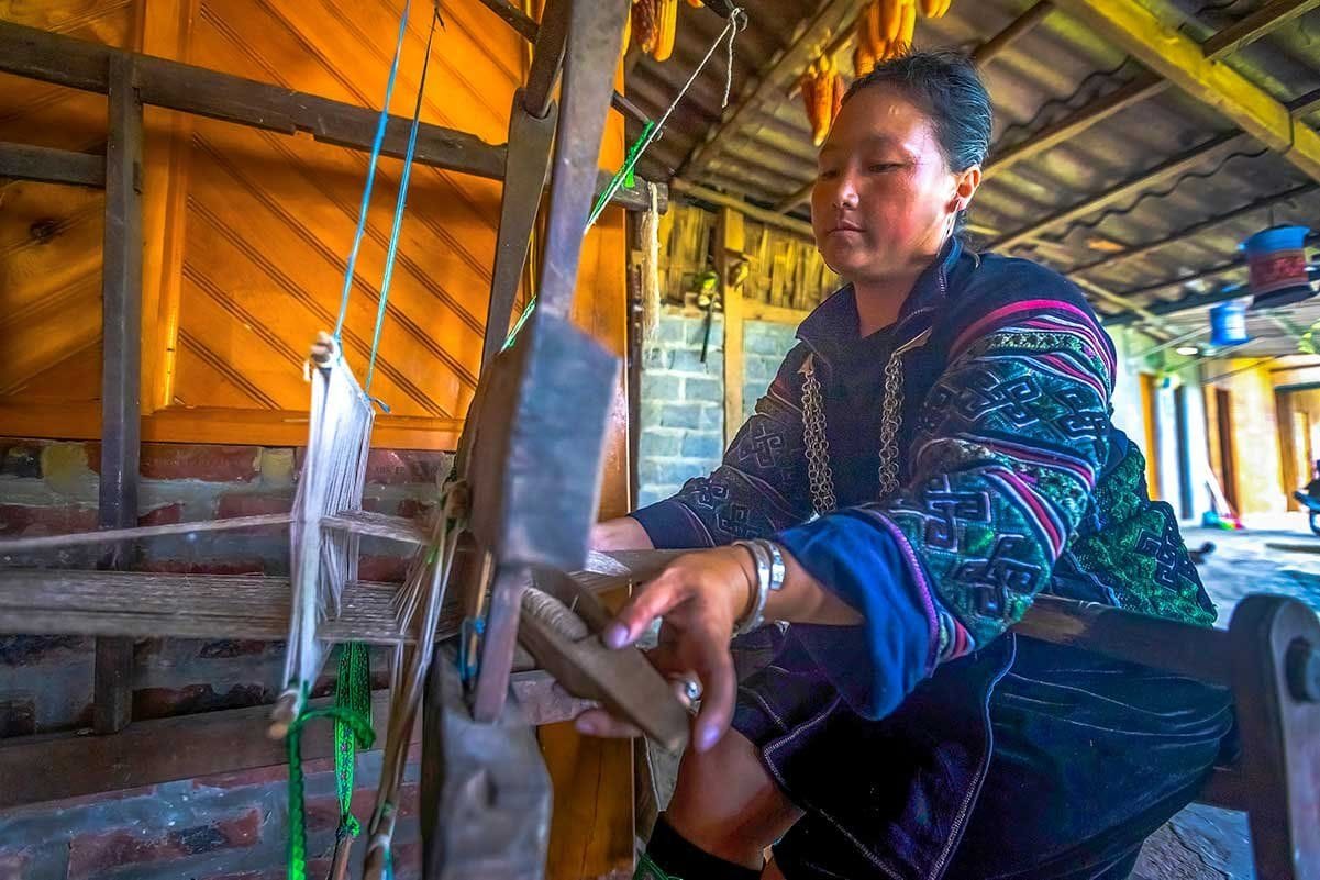A Hmong woman weaving cloth on a wooden loom inside a house in Lao Chai.