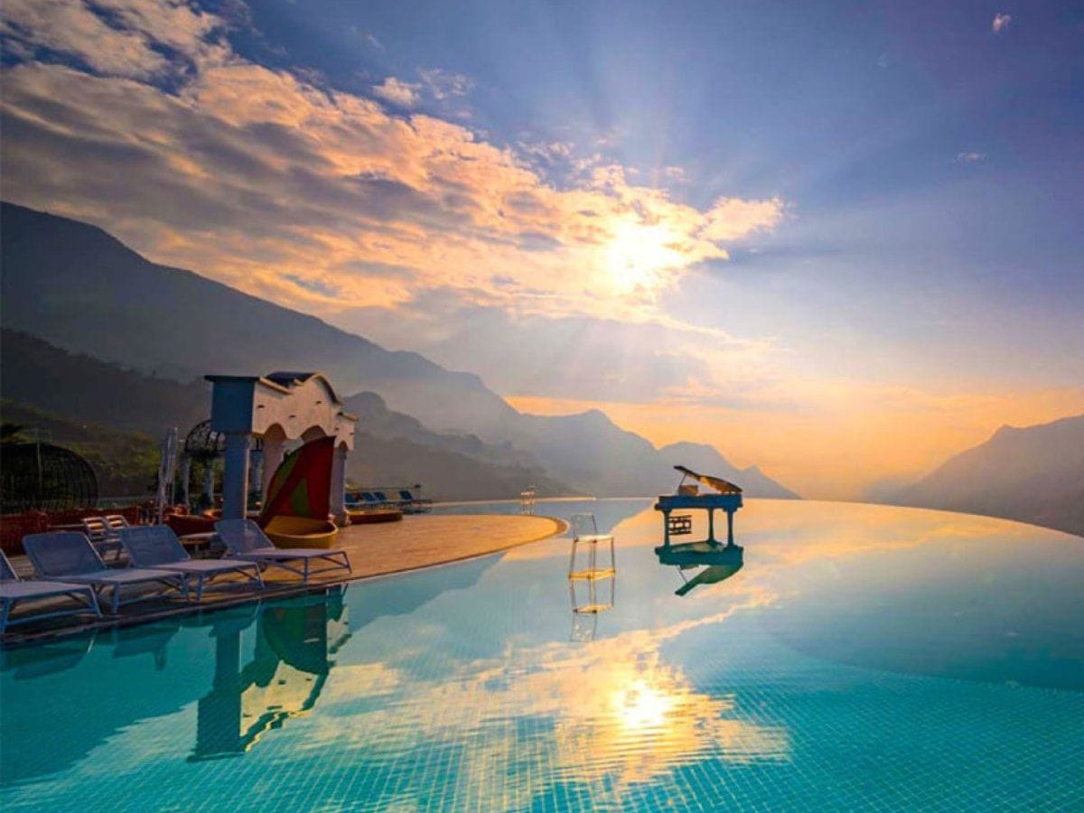 The infinity pool with the white piano standing in the water at sunset.