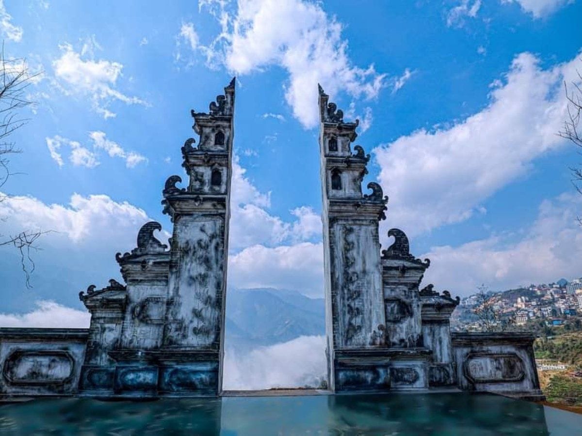 Das Tor im Bali-Stil spiegelt sich im Pool, dahinter Wolken und Berge.