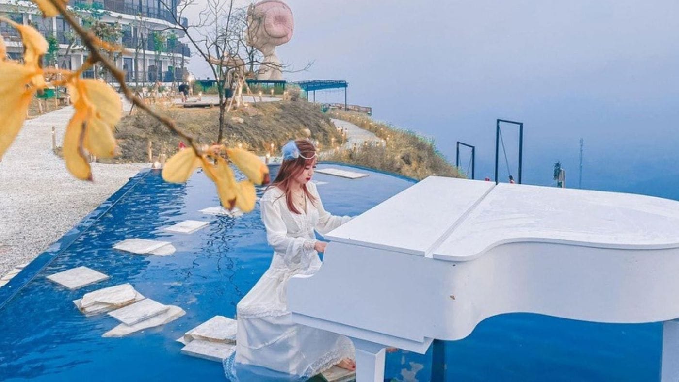 A young woman in white playing the white piano in the infinity pool.
