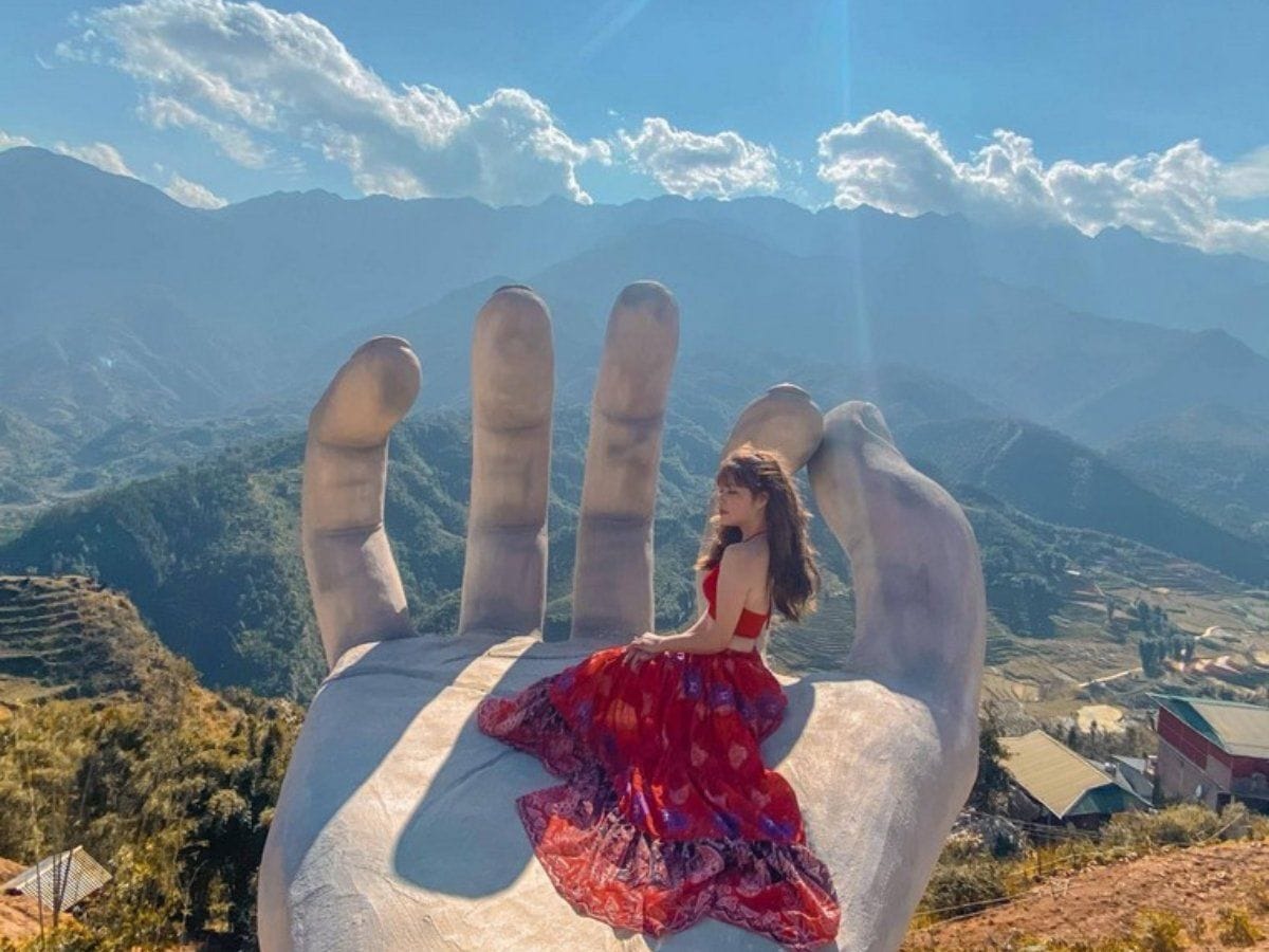 A visitor sitting in the giant hand, looking out over mountains and terraces.