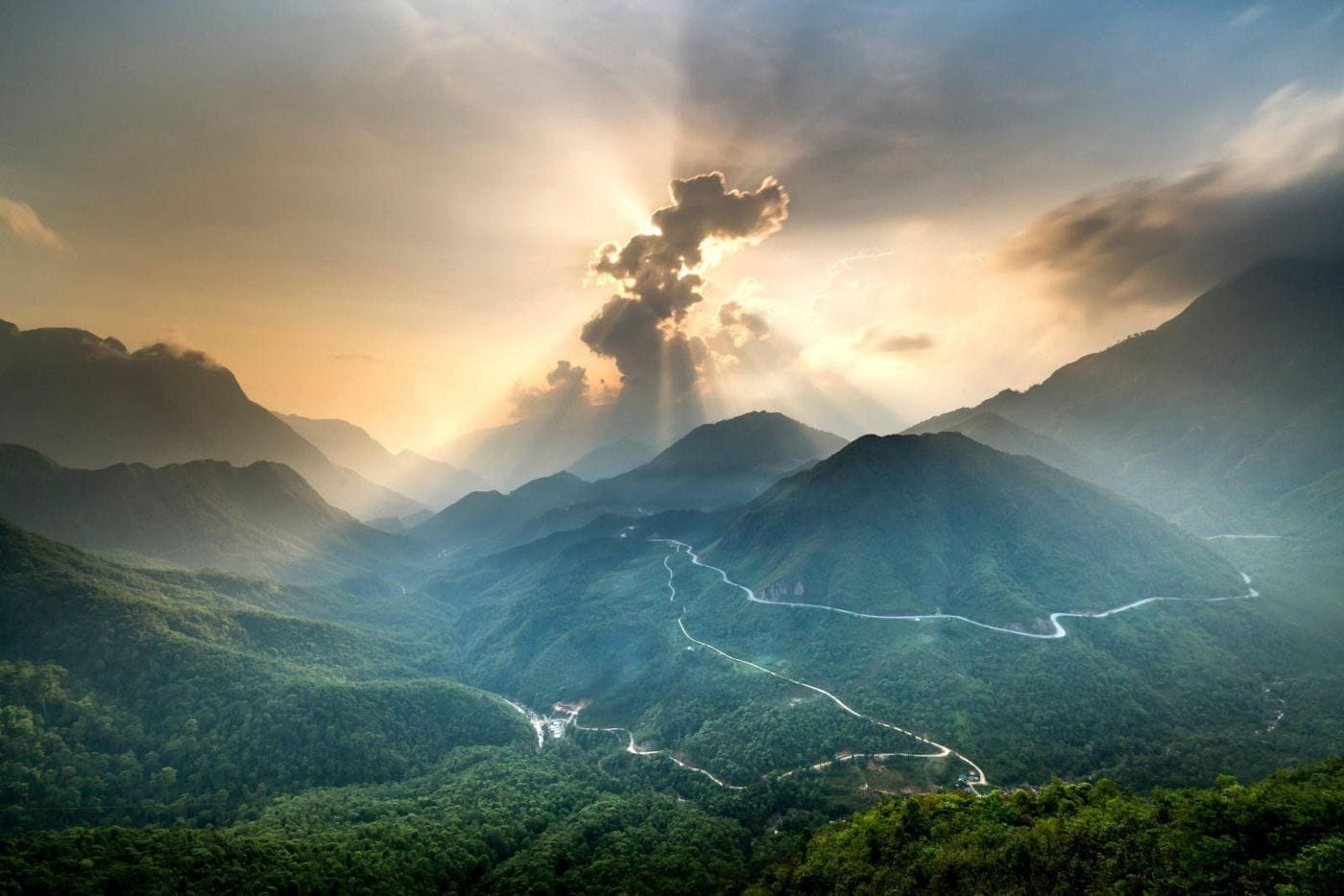 Late-day sunbeams breaking through clouds over the valley, with Ô Quy Hồ pass winding below.