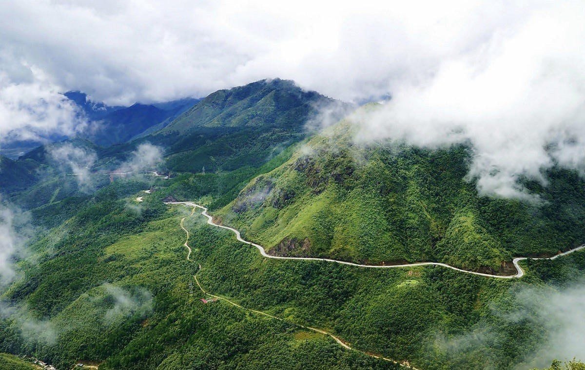 Wolken ziehen über grüne Hänge, die Passstraße durchschneidet das Tal.