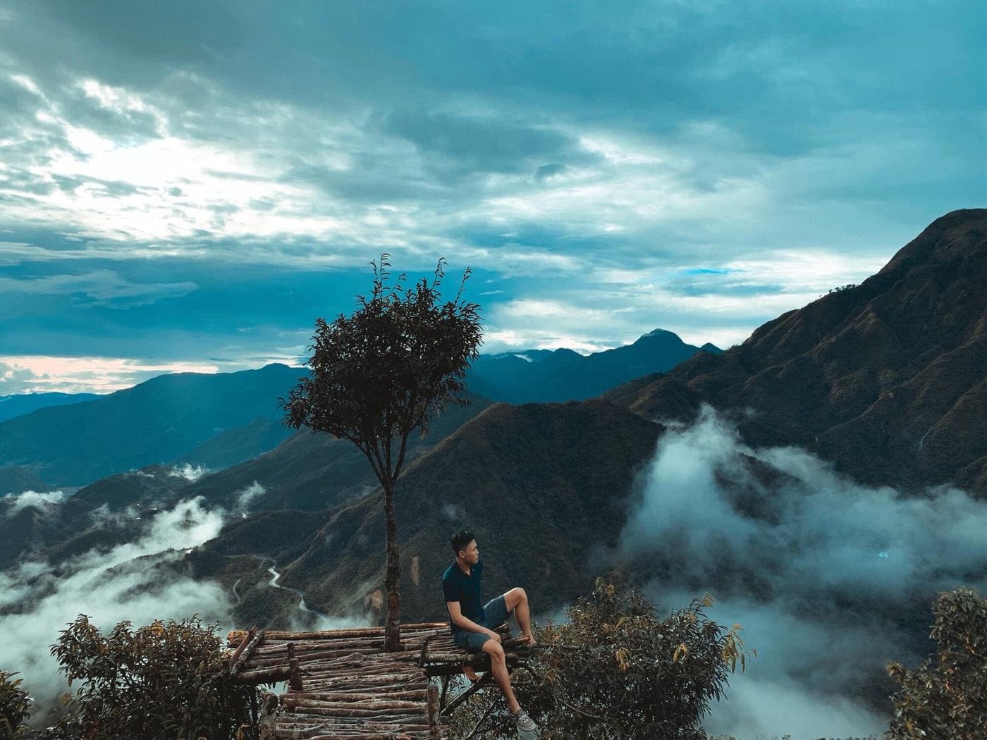 A visitor sitting by the lone tree on the pass, looking over a sea of clouds in the valleys.