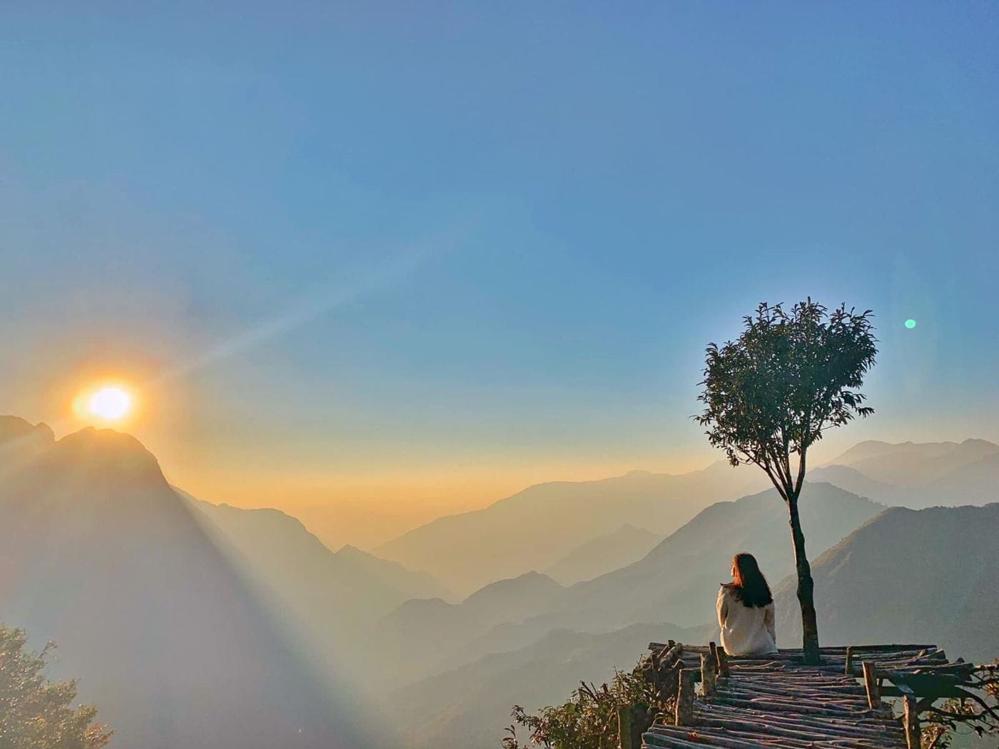 Sunset at the lone tree on Ô Quy Hồ pass, the sun dropping behind layered mountains.