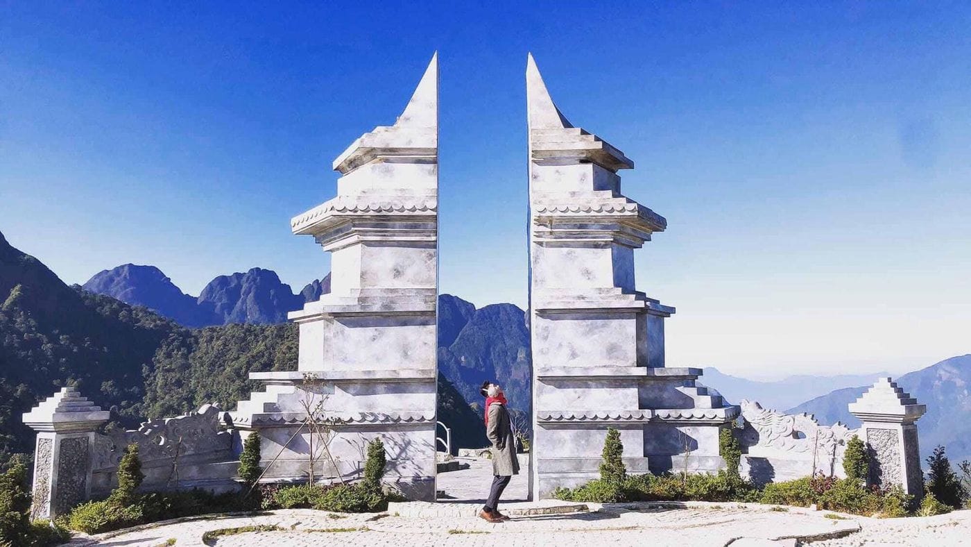 The white Heaven's Gate (Cổng Trời) at Ô Quy Hồ against rocky peaks and blue sky.