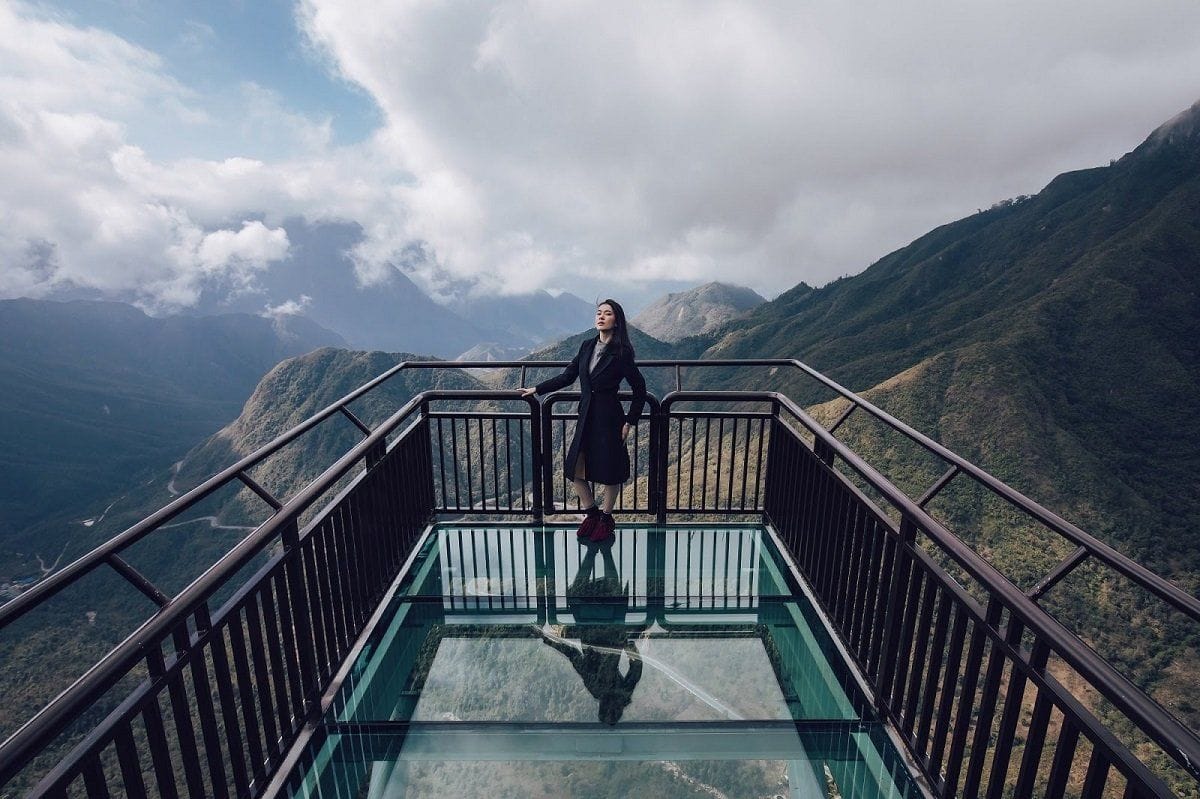 A visitor standing on the transparent glass floor overlooking the Ô Quy Hồ mountains.